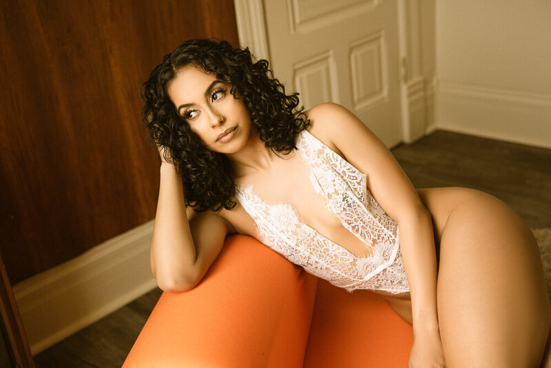 woman posing on orange couch in white bodysuit