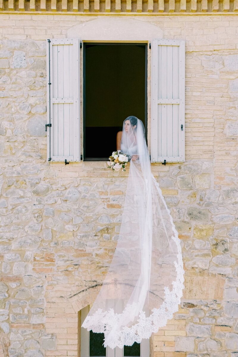 Bride with veil hanging outside window during her Ombroneta wedding in Tuscany.