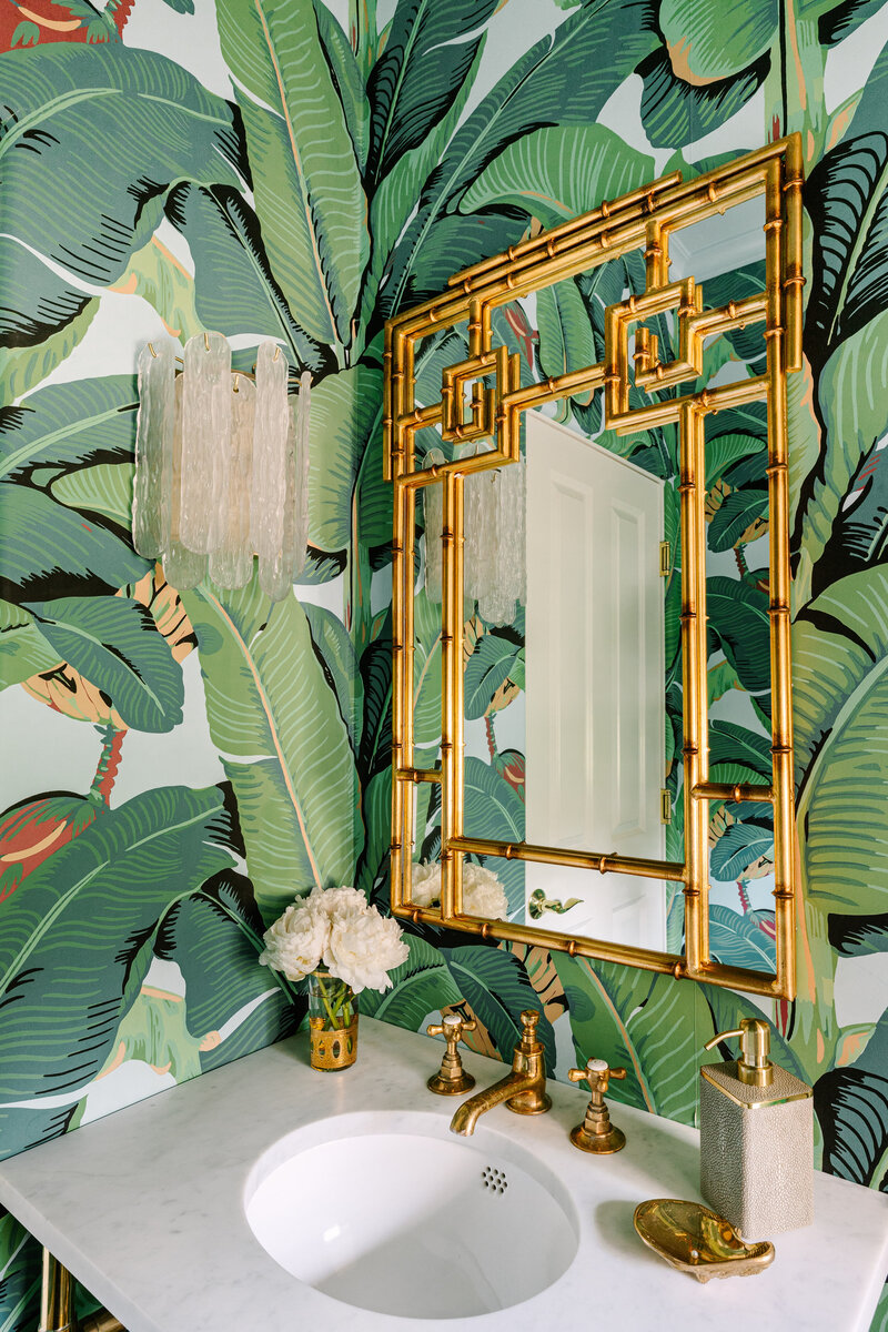 Scalamandre Hinson Palm leaf wallpaper with Hollywood regency brass bamboo mirror and a waterworks crystal, brass, and marble vanity and light blue ceiling.