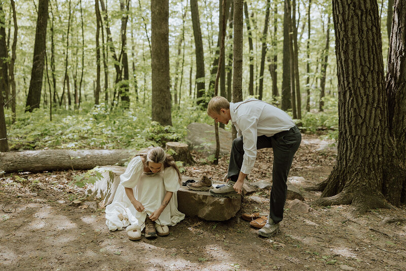Couple putting on hiking boots while getting ready for their elopement in the woods
