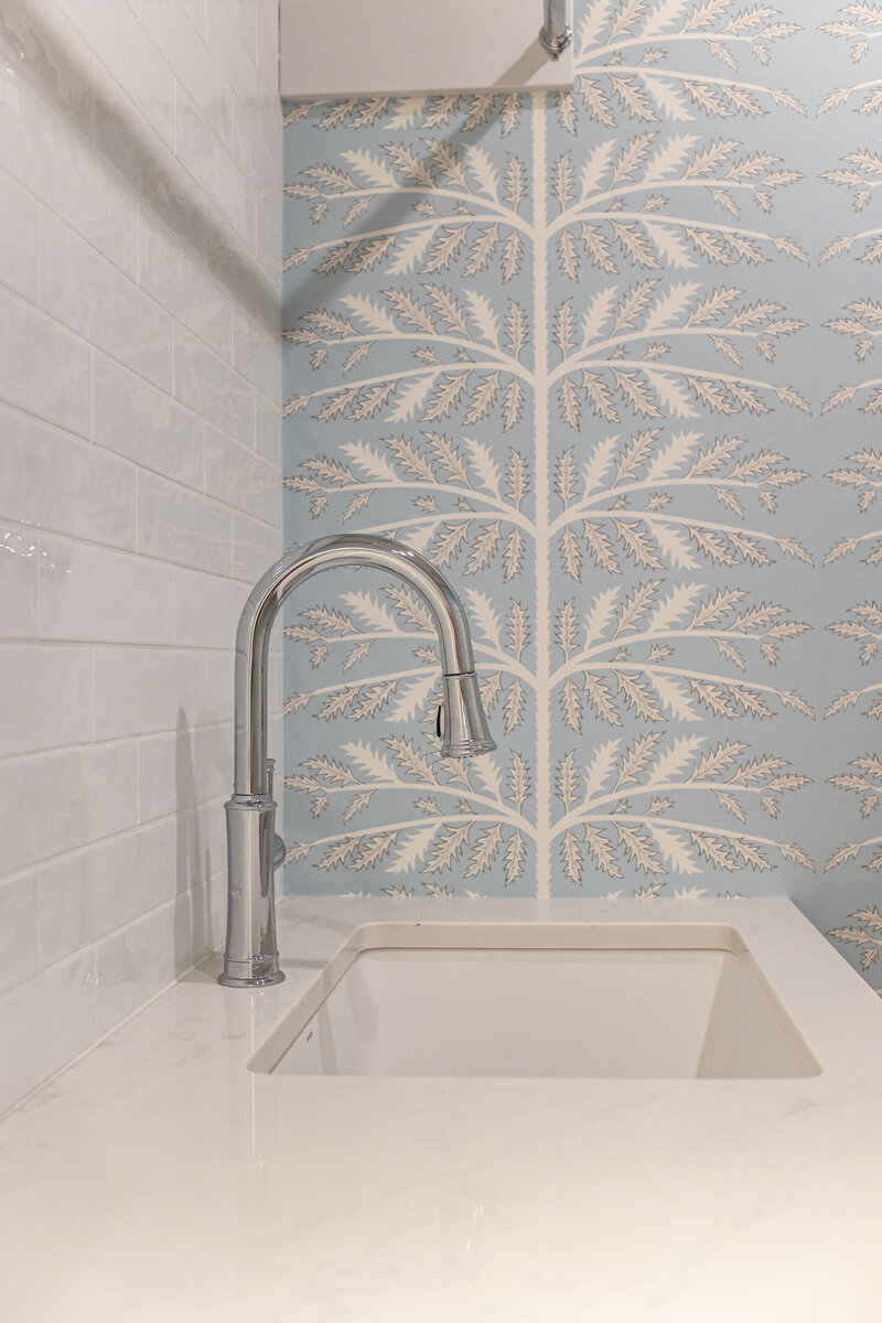 A detailed close-up of a laundry room sink, showcasing custom wallpaper and a beautifully tiled backsplash. The design highlights the attention to detail and style in this functional space.