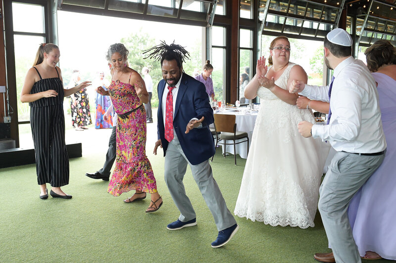 Bride and groom enter their wedding reception with joyful expressions, dancing alongside cheering guests.