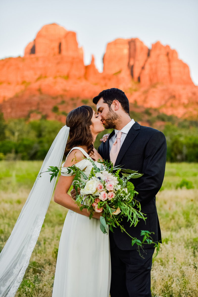 bride and groom kissing with Cathedral Rock background red rocks and green grass at Crescent Moon Ranch Sedona elopement