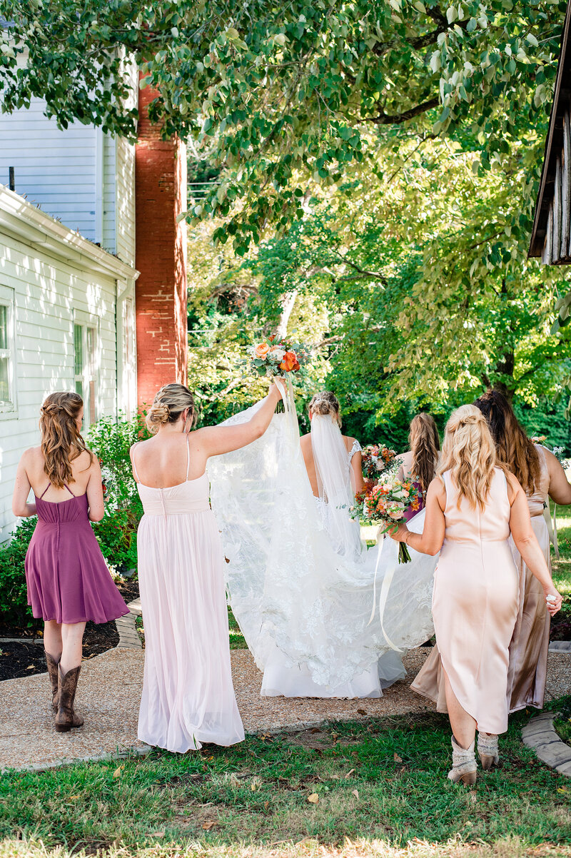 Bridesmaids helping bride with her train and veil walking outside of the wedding venue