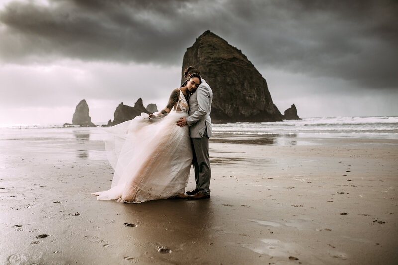 Bride and groom walking along the Oregon Coast with dramatic waves in the background, captured by an Oregon Coast Elopement and Wedding Photographer.