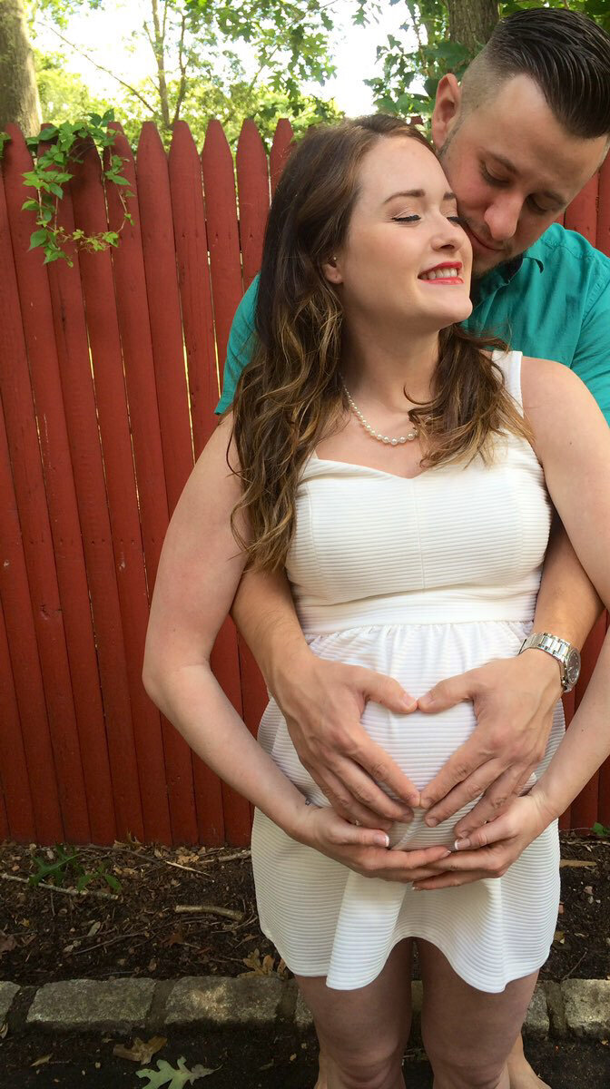 Couple holds pregnant belly forming a heart with hands.