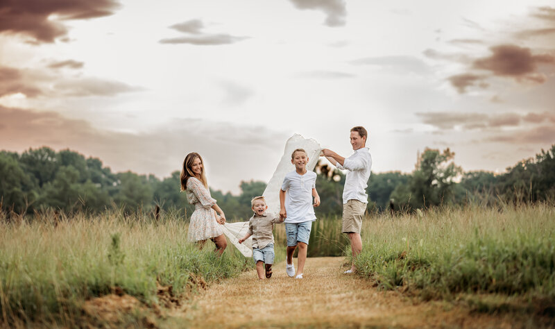 Family of 4 in open field with kids running under a blanket. Photo session taken by Jenni Nikki Photography.