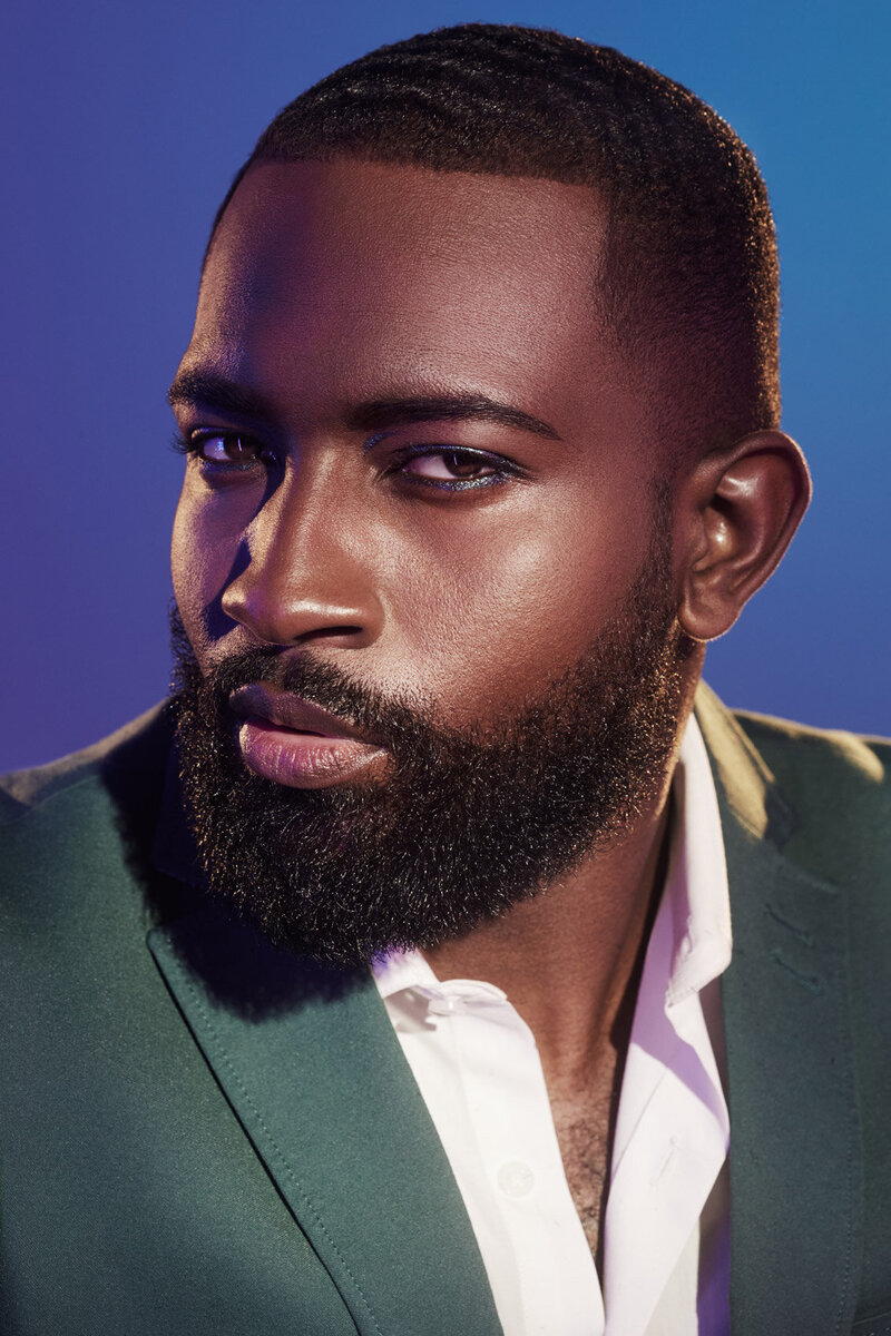 Close-up portrait of Dillard wearing a dark green jacket, with a confident expression against a soft blue background, captured by Ylva Erevall.