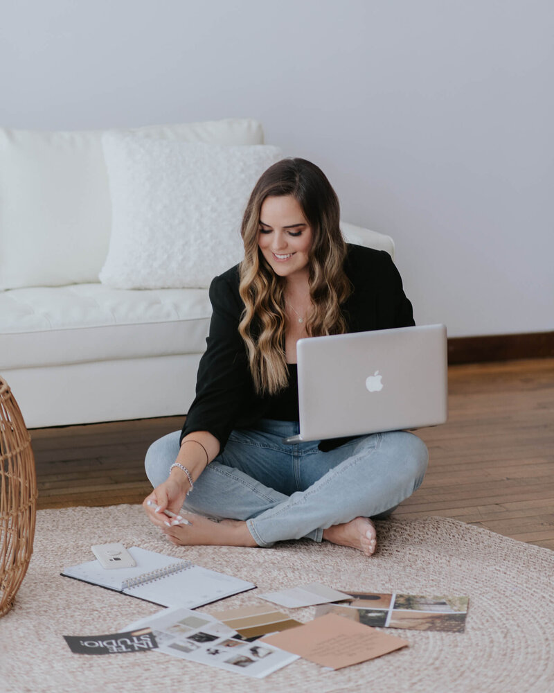 Woman organizing papers on the ground with an open laptop on her lap.