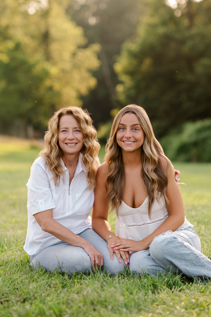 Mom and teen daughter smiling while sitting on the grass during a family photo session in York, PA