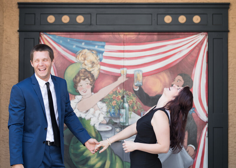 A lively large picture of a couple candidly laughing together in front of a Phoenixville mural, highlighting shared joy.