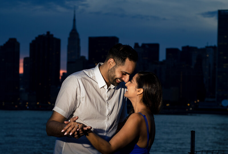 Indian couple enjoying candid moment after marriage proposal after sunset in Gantry with the silhouette of the Empire State Bullding with a hint of sundown.