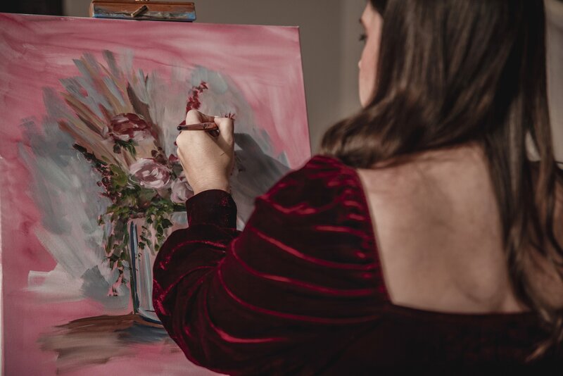 A close up view over Debbie's shoulder as she paints some florals on a canvas