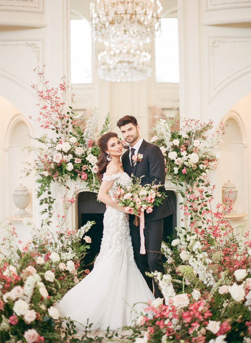 Stunning bride and groom pose for portrait in front of fireplace with elaborate floral installations