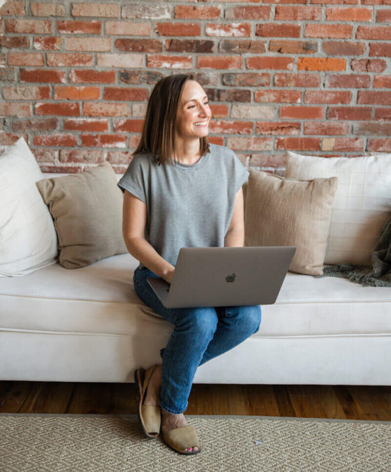 On Brand By Sarah's Social Media Client, Elaine, sitting on a couch that is against a brick wall