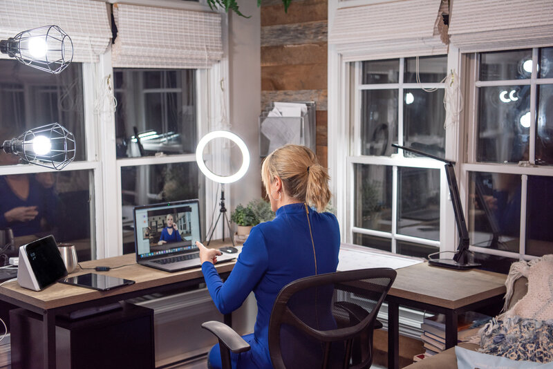 A woman is recording a video in her office and a small ring light.