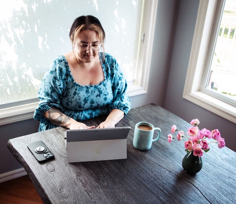 Woman works at a dining room table  with her tablet, phone, and cup of coffee