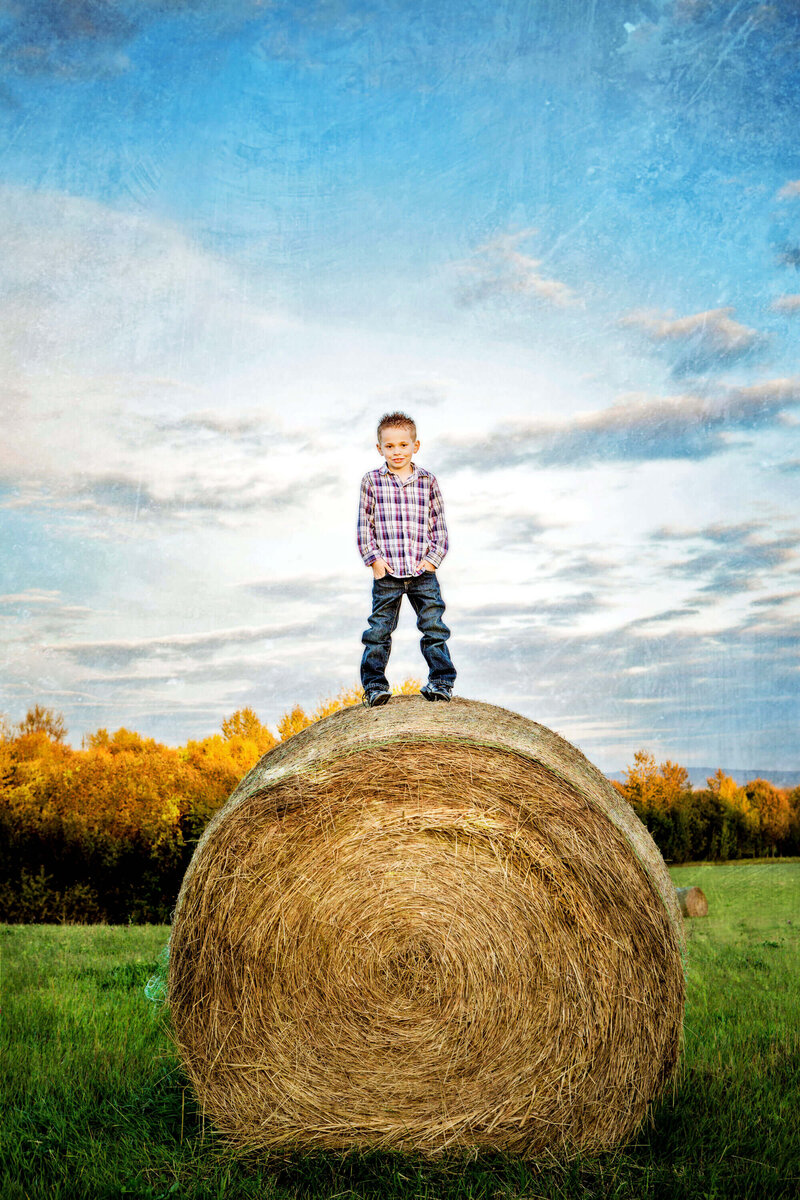 little boy on top of large round hay bale