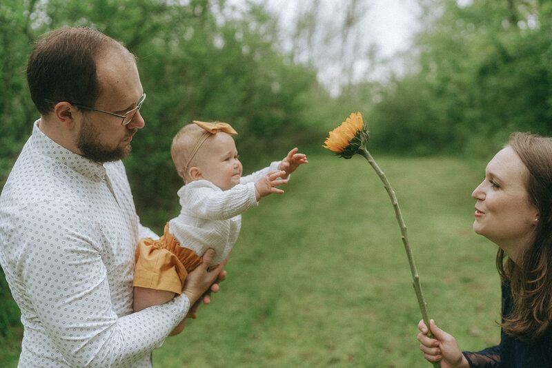 couple holding baby reaching for sunflower during family photoshoot captured by NYC family photographer Elsie Goodman 