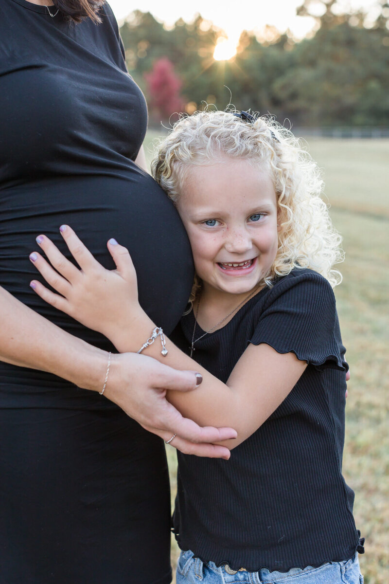 Young girl hugs her mom's pregnant belly during a maternity session