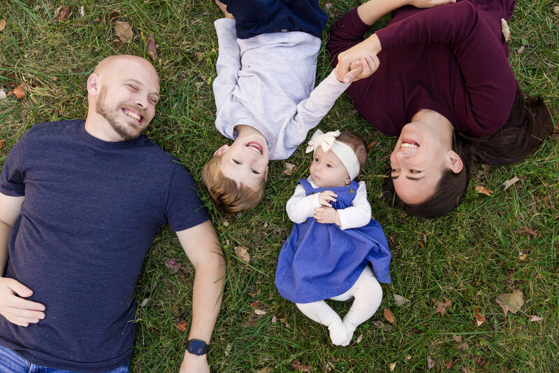 A family of four lying in the grass together, laughing and enjoying time outdoors during a photography mini session in Valley Forge.