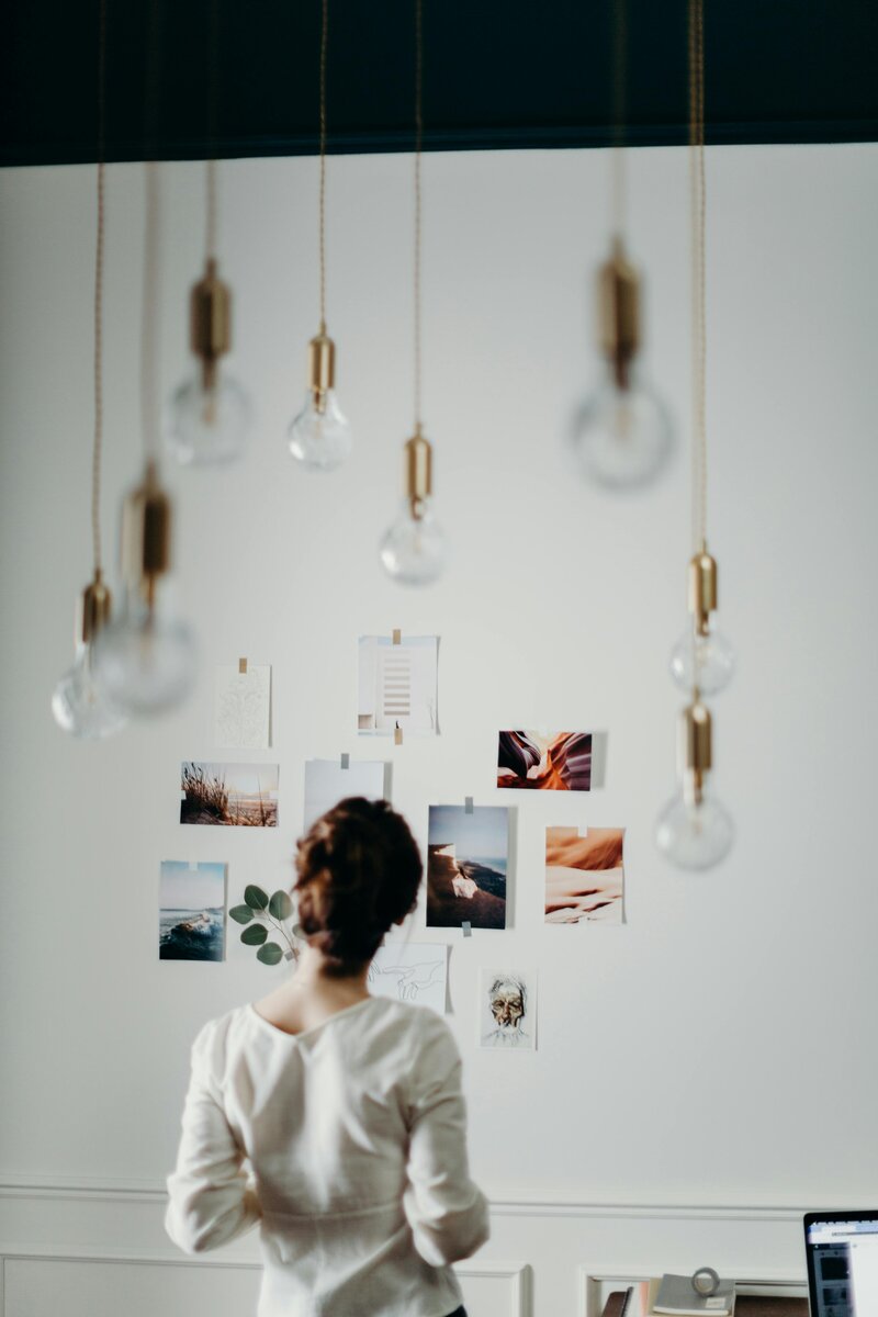 woman looking at images on wall with light bulbs hanging from the ceiling 