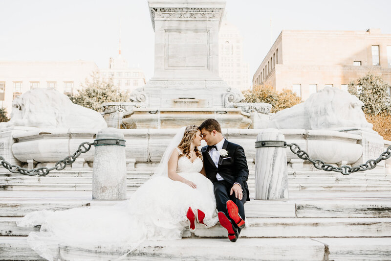 Bride and groom sat in front of monument with red sole shoes