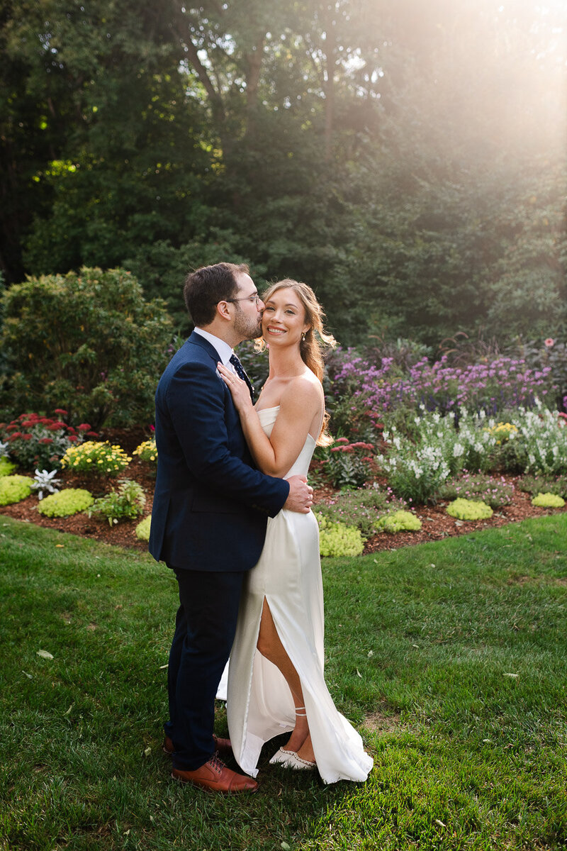 full length bride and groom embrace in garden backlit