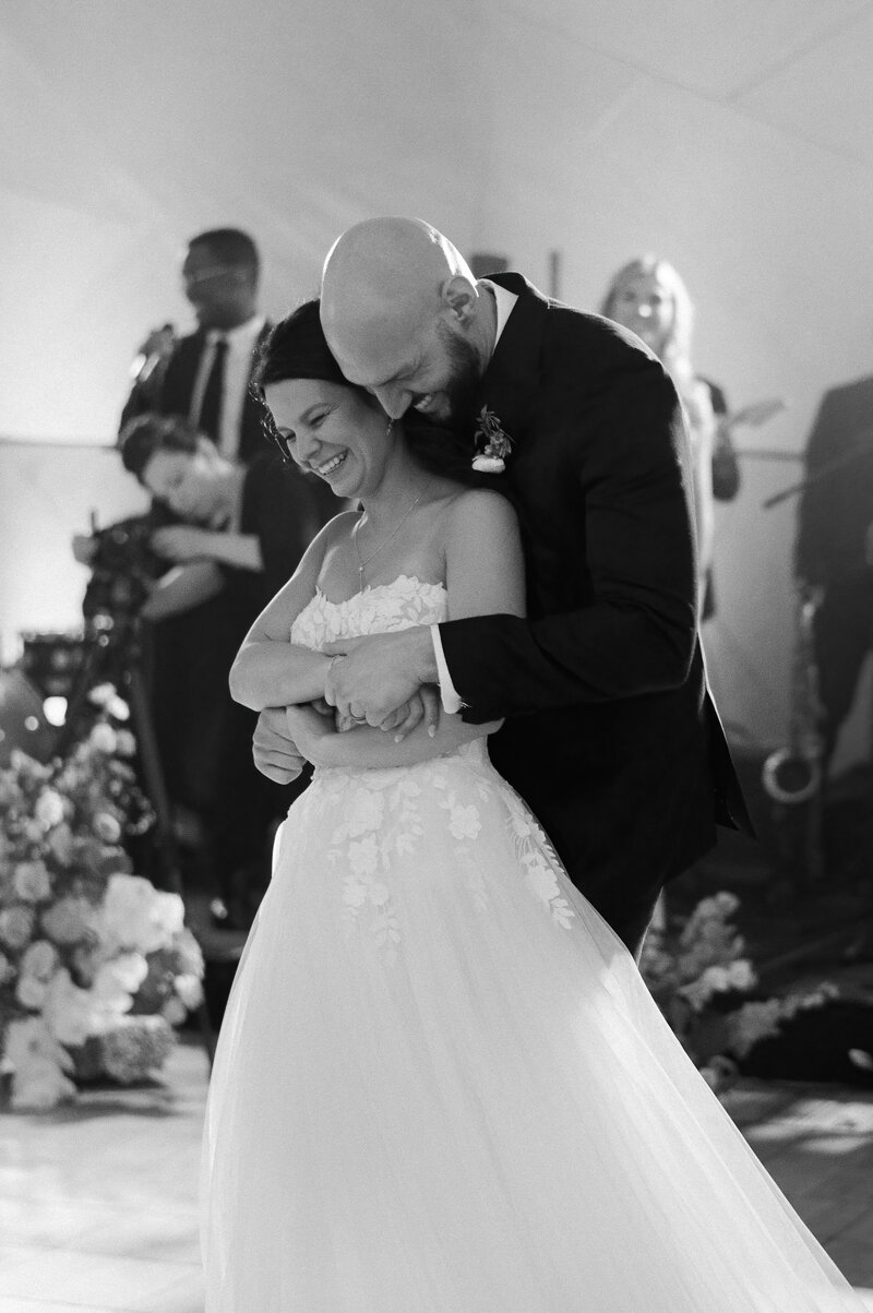 Groom wraps his arms around his bride while they dance together