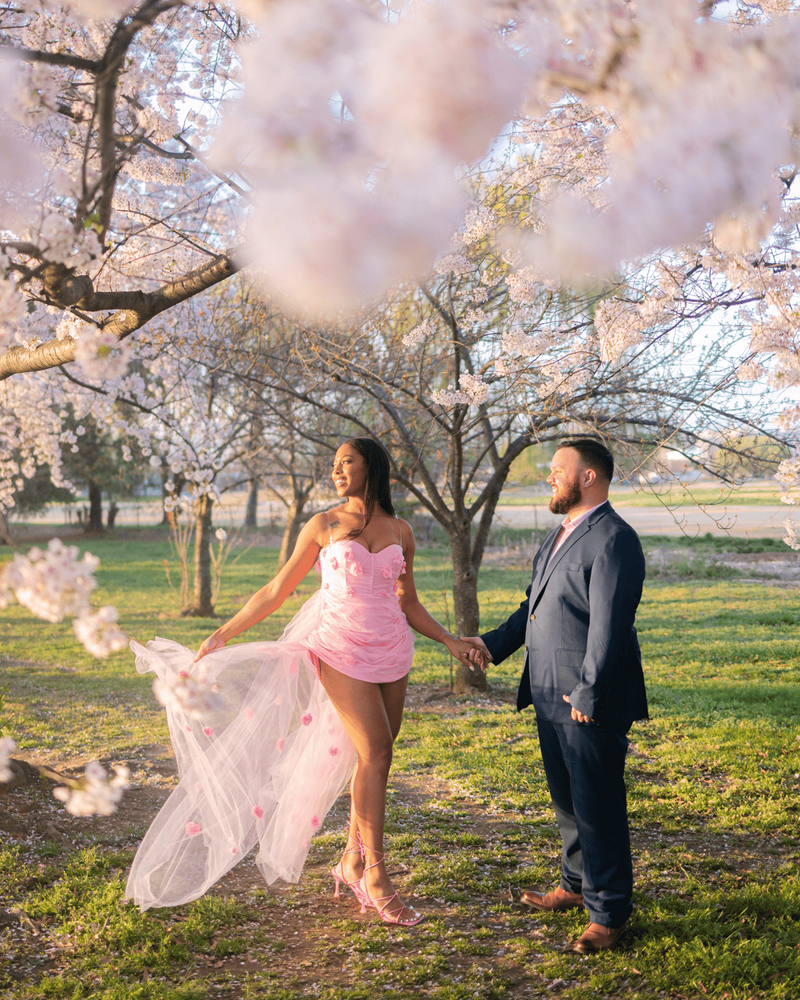 Couple posing for their engagement photos holding hands surrounded by cherry blossom tree in Washington DC. 