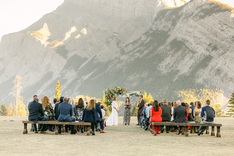 A beautiful summer evening wedding ceremony at Tunnel Mountain Reservoir in Banff, featuring the bride and groom exchanging vows with Mount Rundle as the backdrop.