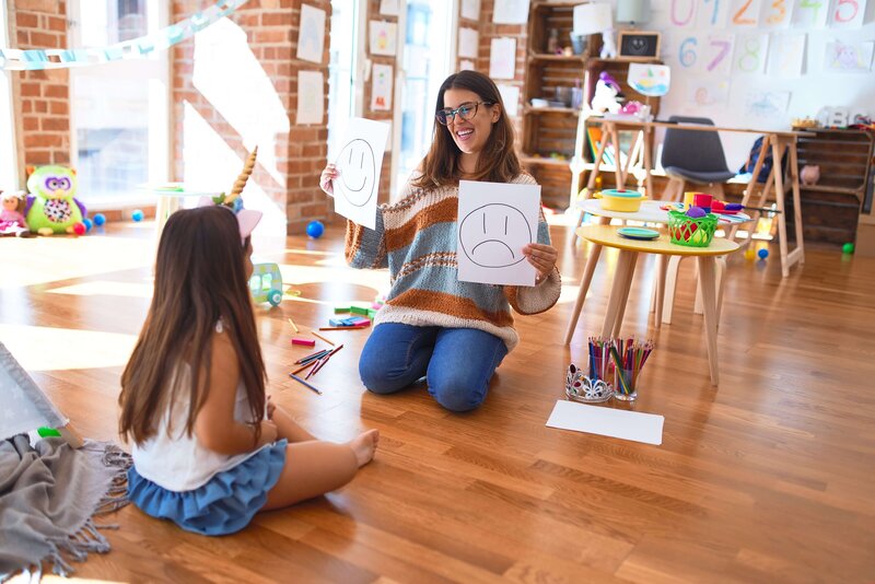 teacher holding a smily face and frowning face pictures to child