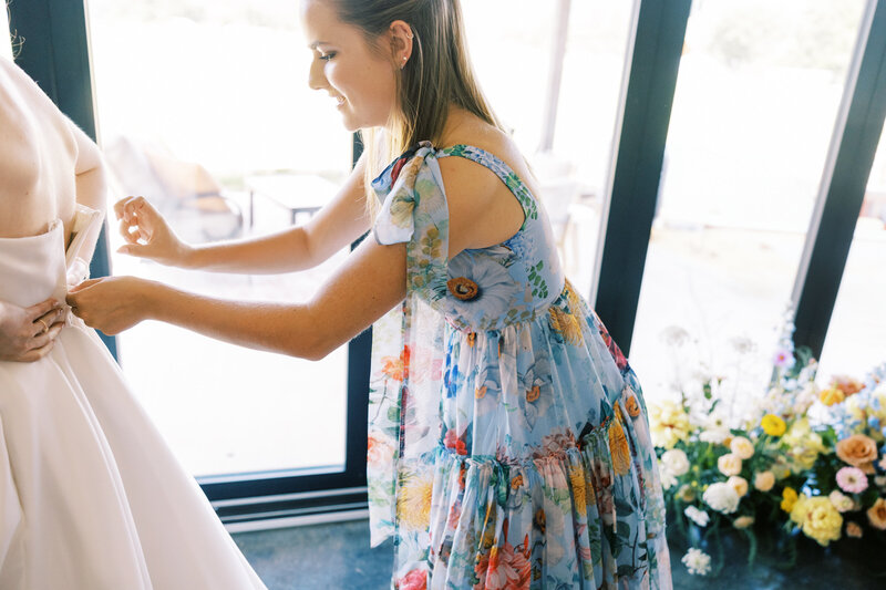 A bridesmaid zips up the bride's wedding dress, captured on film by photographer Megan Lynn of My Sun and Stars Co.