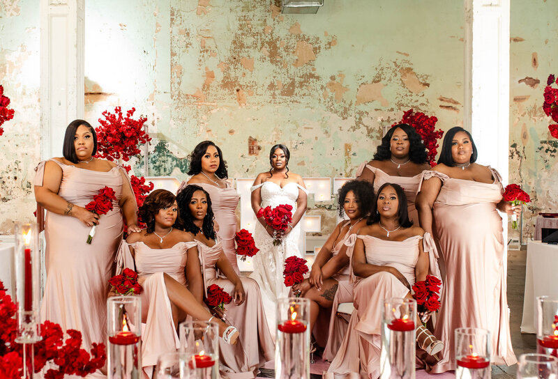 Stunning image of a bride and her seven bridesmaids, all in pink gowns with red flowers. Makeup by Esthetized by Nadia, showcasing beautiful decor by Opulence Events at 701 Whaley Street. Perfect for capturing the essence of a luxurious wedding celebration.