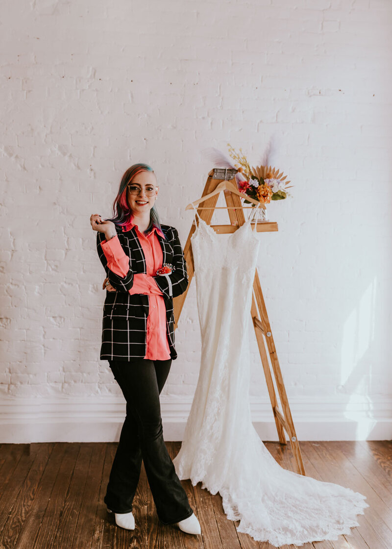 Designer standing next to a lace wedding dress hanging on a wooden ladder