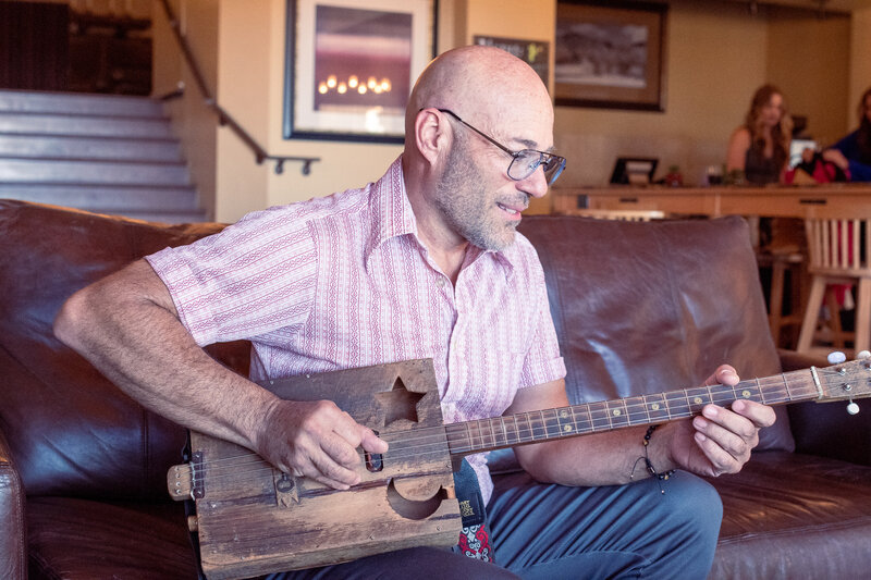 Smiling man playing a handmade wooden guitar indoors, photographed by Vyrl Photo, showcasing Tucson brand photography.