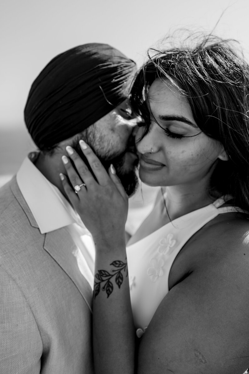 Black and white close up photo of the man kissing the woman on the cheek with her hand on his cheek with her engagement ring in view captured by Zanthe Vorsatz Photography