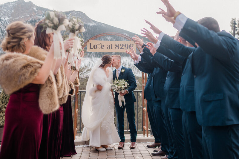 Bride and Groom kiss each other while their bridesmaids and groomsmen cheer on either side of the them.