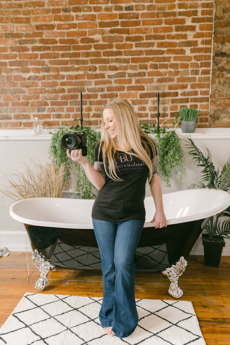 A woman standing in front of a tub holding a camera.