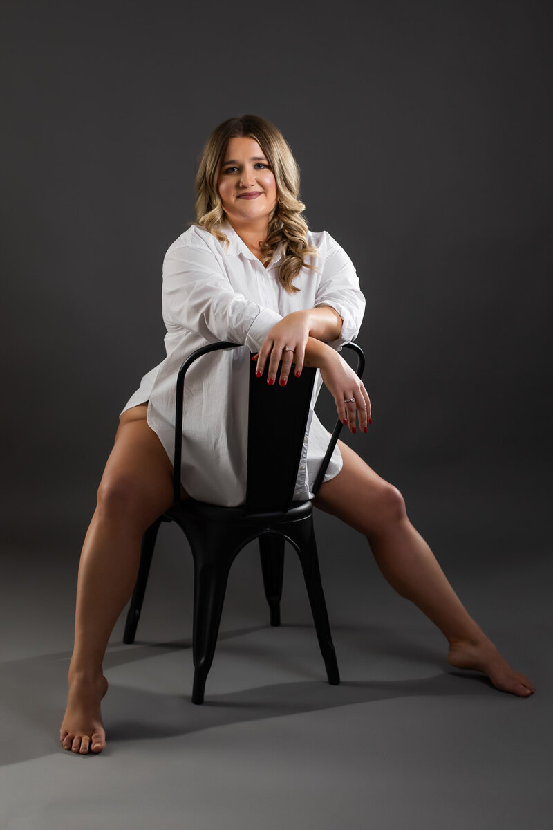 A woman in her 50s is kneeling on the ground facing a sofa while wearing lingerie