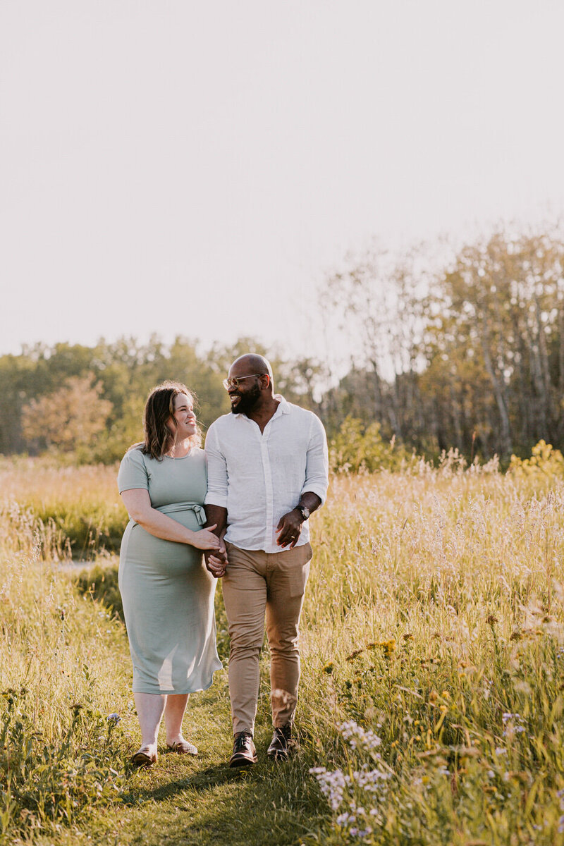 Couple holding hands walking in the fields at Assiniboine Forest for maternity photos 