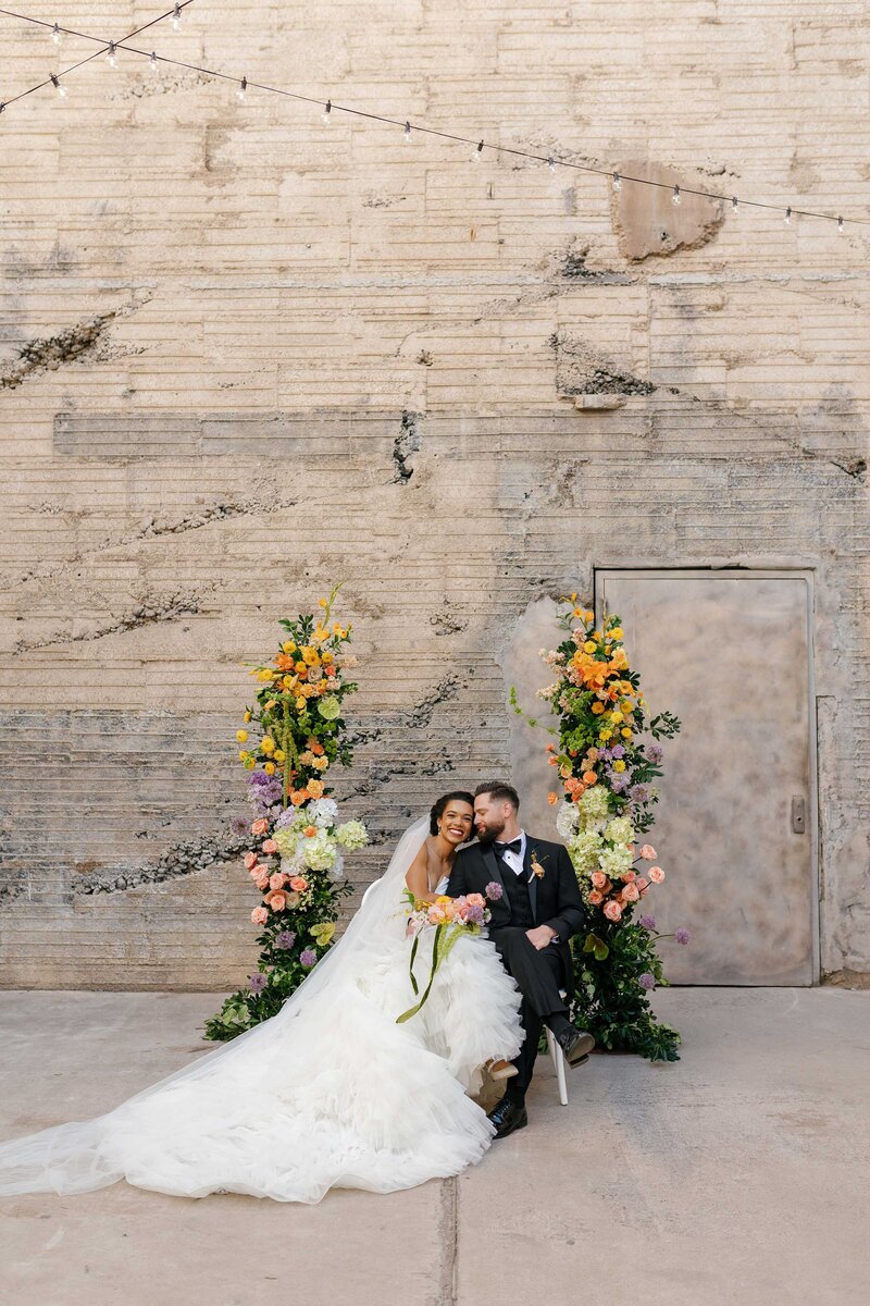 Bride and groom cuddle while sitting together between colorful archway.