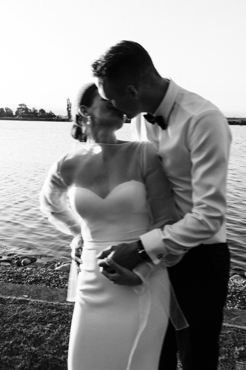 blurry black and white photo of a bride and groom in trish peng dress kissing at sunset beside a lake