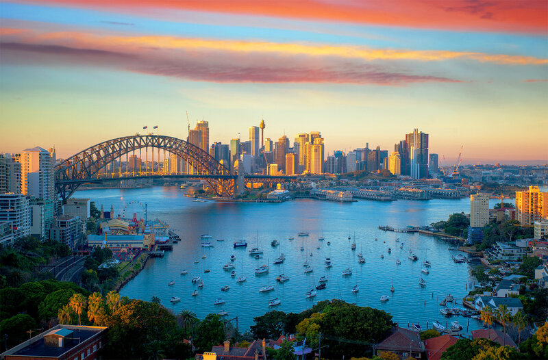 View of Sydney Harbour with the Sydney Harbour Bridge, city skyline, and boats on the water at sunset.