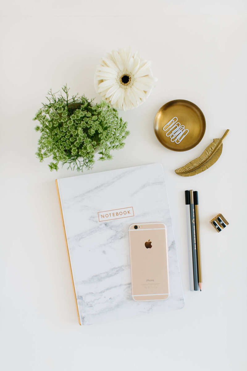 Modern desk flatlay with a marbled notebook, gold accessories and  a small plant.
