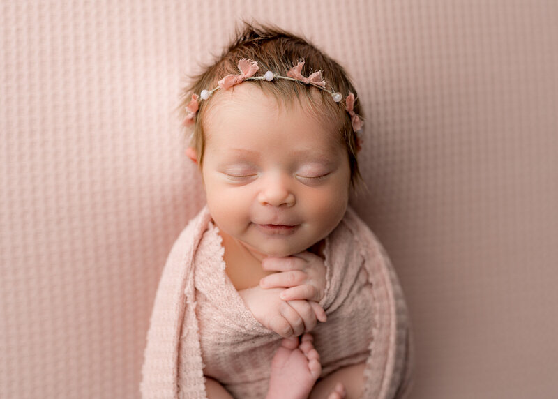 newborn baby girl wearing a pink bow headband wearing a pink swaddle blanket