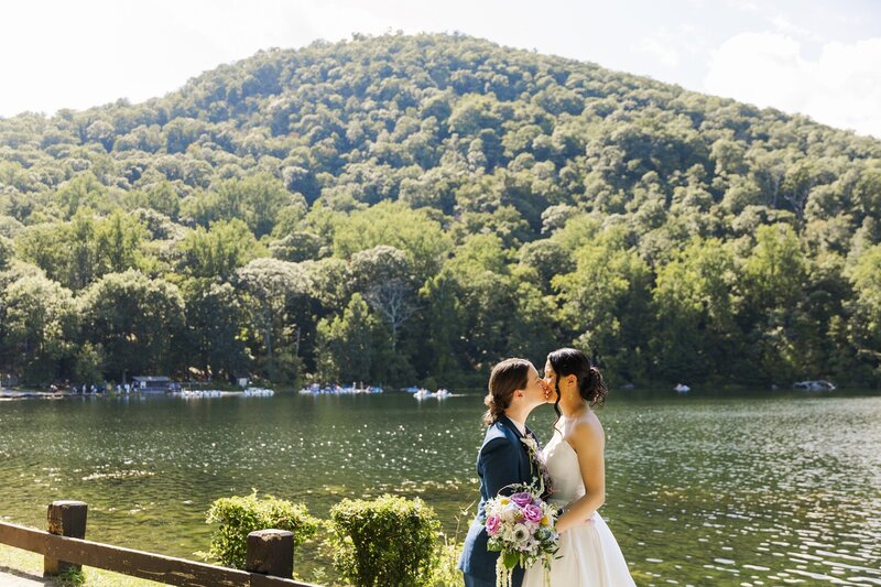 Couple standing close beside a lake with forested hills behind them