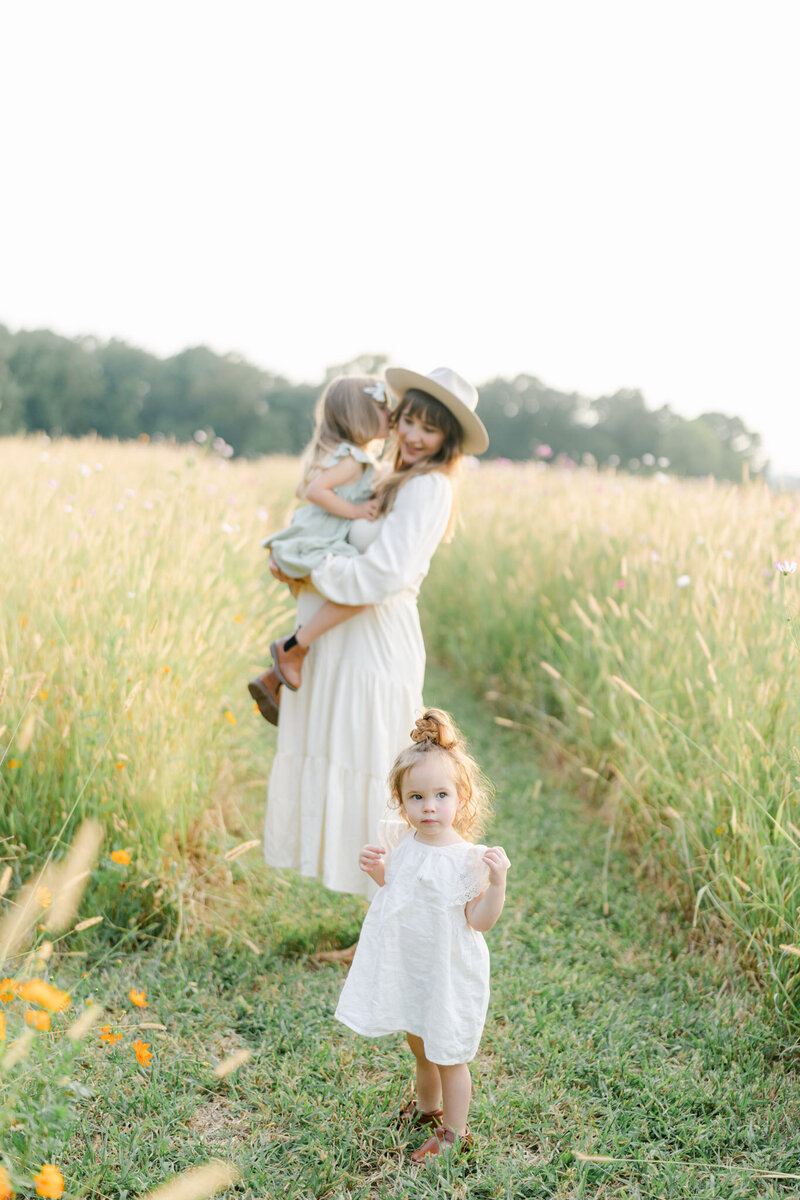 Mother and daughters in white dresses stand in a field of golden tall grass at sunset in Lancaster County, PA