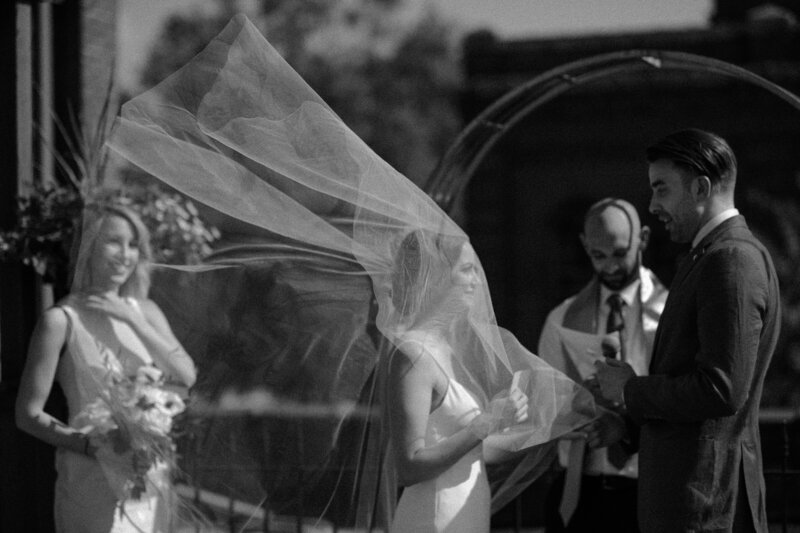 a bride's veil blows up dramatically in the wind during the wedding ceremony