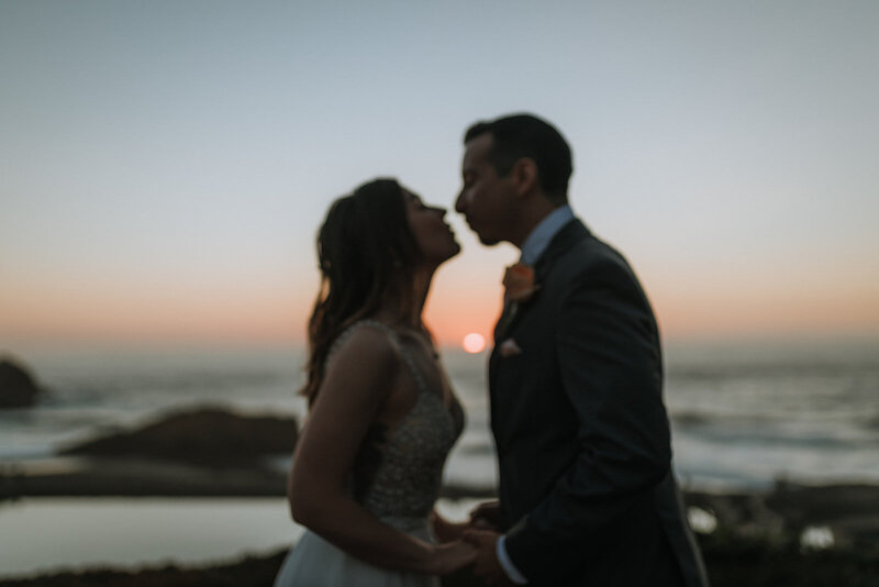 Bride and groom kissing with the sun going down and the ocean behind them